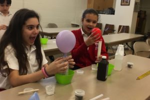 Two girls are playing with a balloon in the middle of a table.