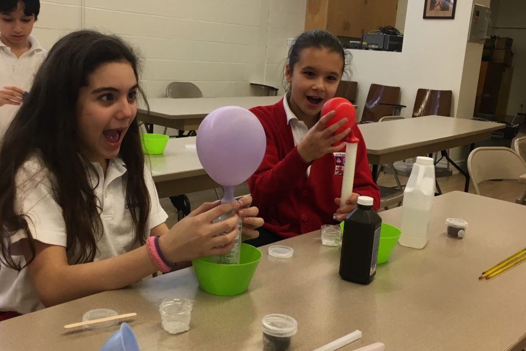 Two girls are playing with a balloon in the middle of a table.