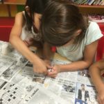 Two girls are playing with a newspaper puzzle.