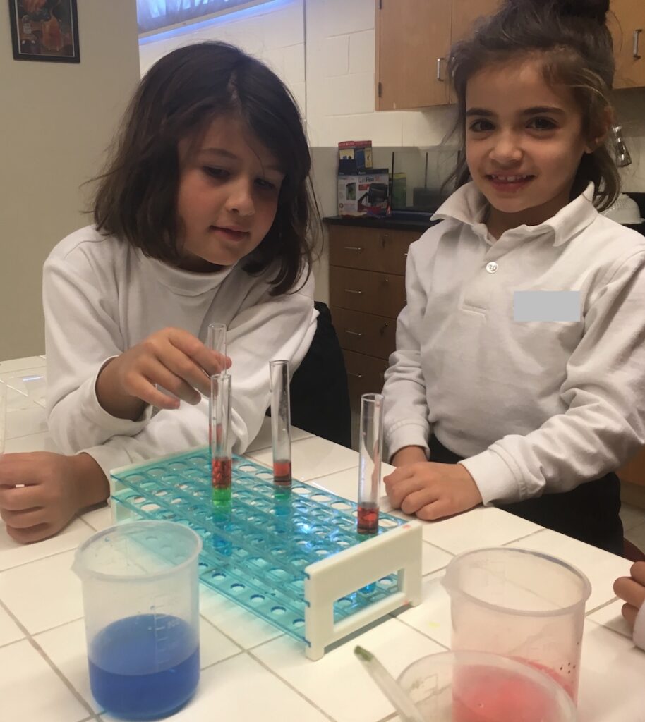 Two girls are playing a game with water and test tubes.