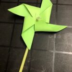 A green paper windmill sitting on top of a floor.