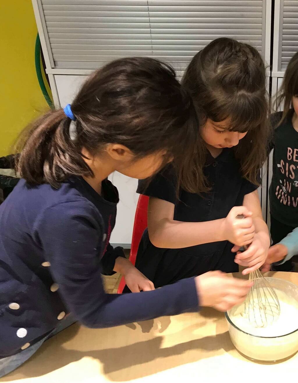 Three girls are making a cake together.