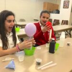 Two girls sitting at a table with balloons and cups.