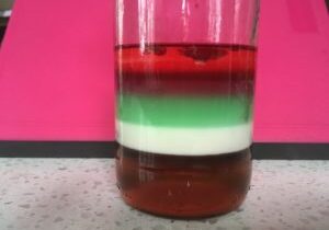 A glass of liquid with red, green and white layers.